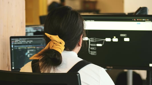 Woman with yellow hair tie facing desktop computer screen with a workflow mapped on it.