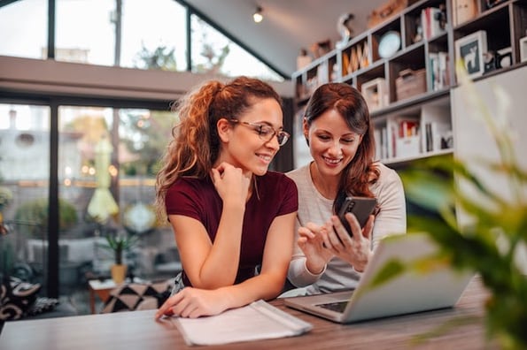 two people using a laptop and smartphone to find wordpress auction plugins