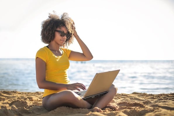 person using a laptop on the beach to manage a website on holiday