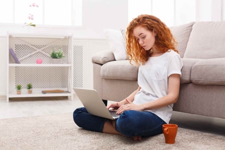 woman sitting on a carpet and visiting an accessible website. The woman is wearing a t-shirt and jeans