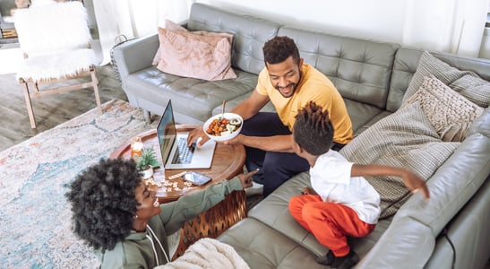 A family of three gathered around a laptop on their L-shaped couch