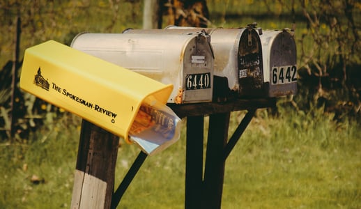 Three closed tin mailboxes and one jarring yellow plastic mailbox stuffed full of adverts and junk mail