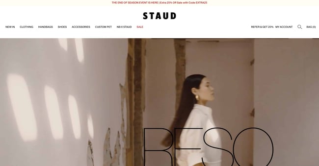 fashion website design staud shows person against a netural wall wearing products