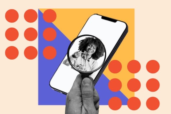 A person holds a magnifying glass over a smartphone that's playing a video of an influencer.