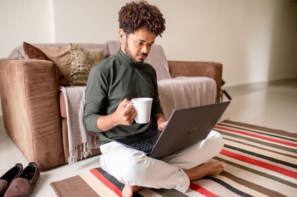 Person looking into accessibility issues on their website sitting on the floor of their apartment with laptop and cup of coffee. 