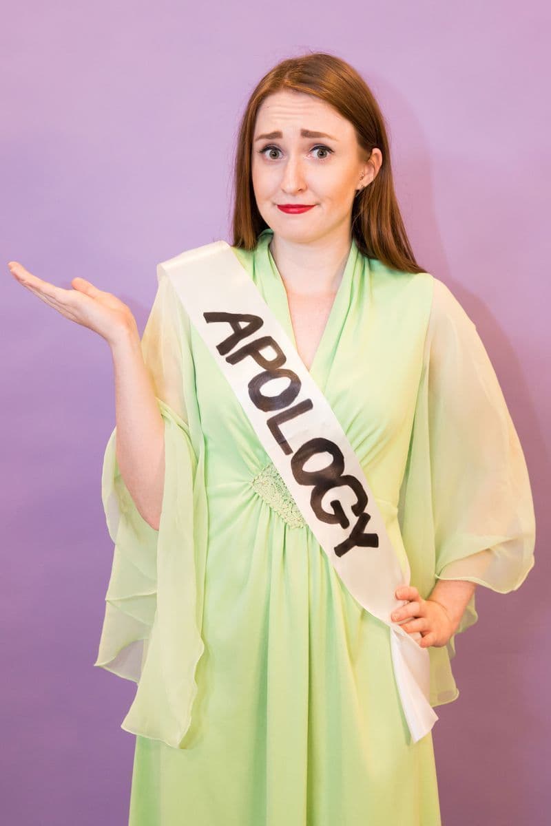 Woman wearing formal gown with a sash that says "apology."