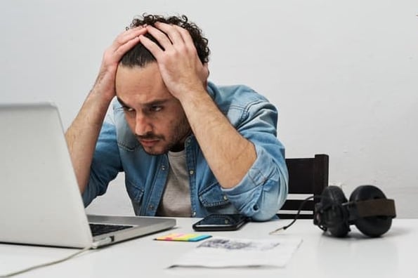 Man stares at laptop with his hands on his head as he deals with burnout