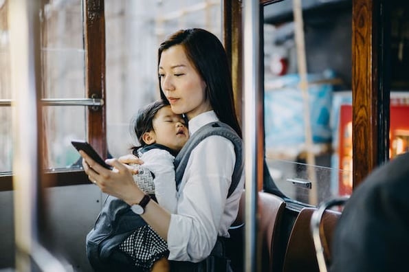 woman holding a baby on train while using chatbot from her phone