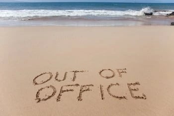'out of office' written in sand on beach