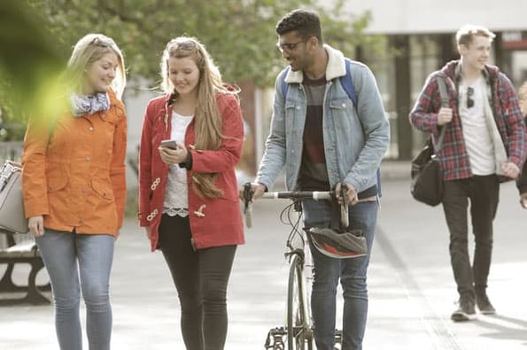 Gen Z students look at one of their friend's iphones as they walk to class aimed to debunk gen z myths.