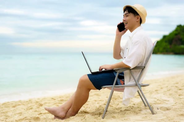 Man on the beach taking phone calls and performing holiday website management for his small business