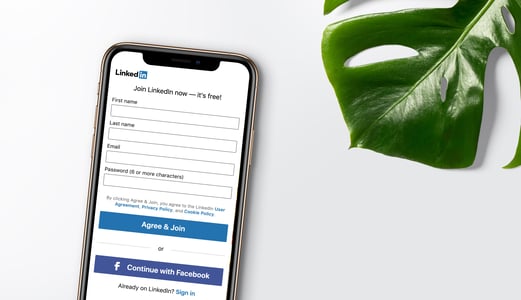 Phone showing LinkedIn signup screen next to a dark green leaf