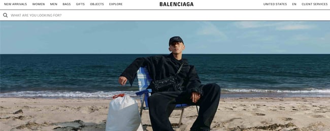 Luxury websites: Balenciaga. Features a person wearing Balenciaga apparel sitting on the beach. 
