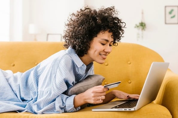 A woman holding a credit card is on her laptop and looking at product attributions before making a purchase.