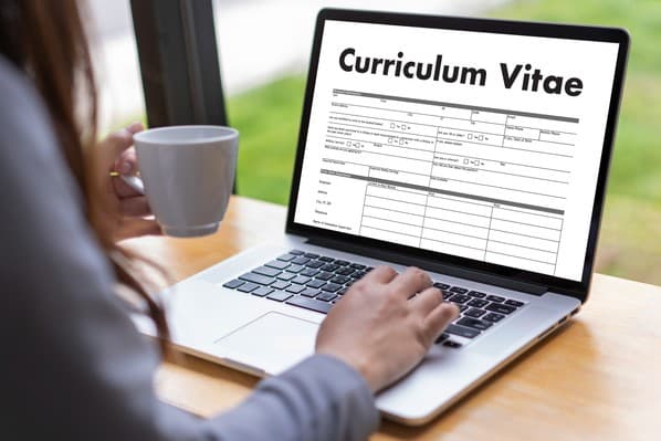 A woman uses her laptop to complete her curriculum vitae. The word curriculum vitae appears on the laptop screen.