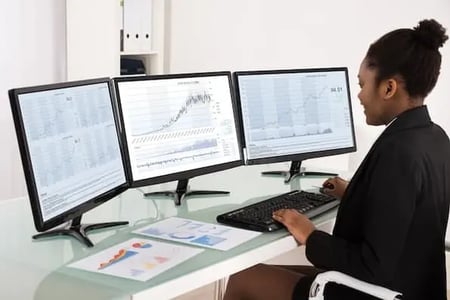 marketer at desk with three monitors using tactics for better sales forecasting