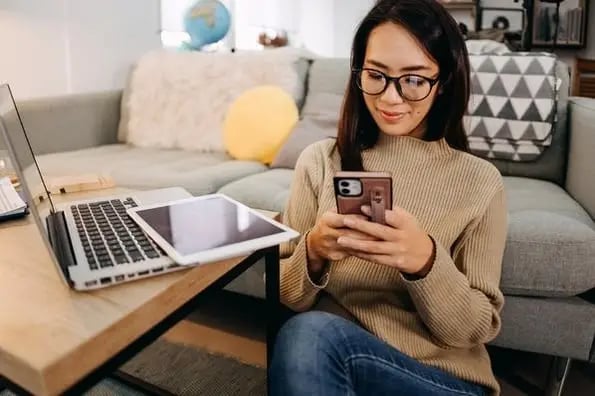 Using Slack tips, a woman uses both her laptop and mobile phone to communicate remotely.