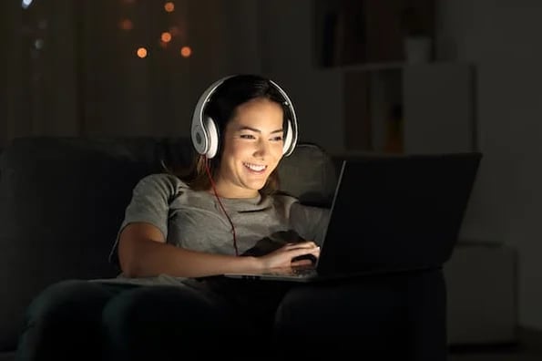 woman on laptop in the dark smiling as she watches snackable content