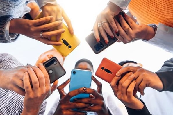 A group of people huddle together to look at their smartphones