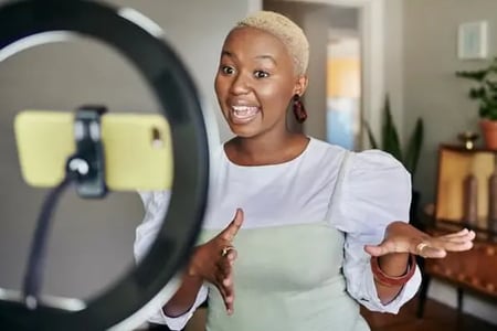 A woman records social media content on her smartphone, which is attached to a ring light; social media metrics