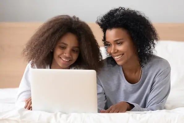 two people lying on a bed watching a video on a video hosting site