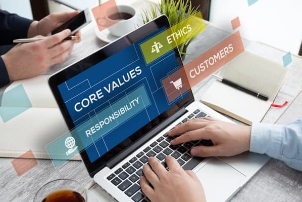 A hand is typing at a computer that has a screen that reads "core values," "ethics," and "responsibility." The image represents a brand manifesto.